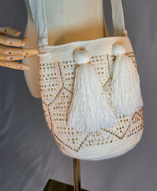 A cream-colored crocheted shoulder bag with two large tassel details, displayed on a cream fabric mannequin torso.