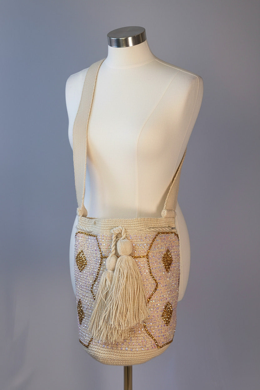 A cream and gold beaded shoulder bag with a tassel, displayed on a wooden-arm mannequin torso against a light gray background.